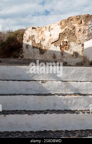 Treppe weiß von der Seite und schwarze Steinstruktur oben. Alter verwitterter Zaun mit abgespaltener Fassade im Hintergrund. Intensive weiße Wolken auf Stockfoto