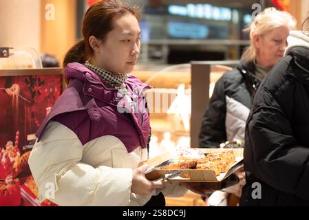 Im Einkaufszentrum steht eine junge Chinesin in der Schlange und wartet darauf, für das Essen, den Kuchen und die Torten zu bezahlen, die sie bestellt hat Stockfoto