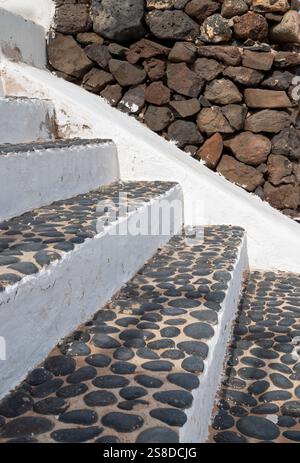 Treppe weiß von der Seite und schwarze Steinstruktur oben. Alter verwitterter Zaun mit abgespaltener Fassade im Hintergrund. Intensive weiße Wolken auf Stockfoto