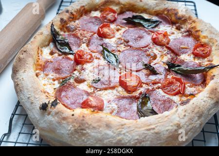 Rohe Peperoni-Pizza ist fertig zum Kochen. Pizza mit Wurst, Tomaten, Käse und Basilikum auf einem Backrost. Hochwertige Fotos Stockfoto