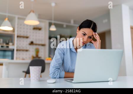Gestresste Geschäftsfrau mit Kopfschmerzen, die von zu Hause aus auf einem Laptop arbeitet und müde und überfordert aussieht Stockfoto