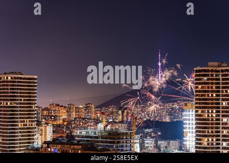 Ein lebhaftes Feuerwerk erleuchtet den Nachthimmel über der Innenstadt von Tiflis, Georgia, mit Wolkenkratzern im Vordergrund. Die festliche Atmosphäre unterstreicht das c Stockfoto