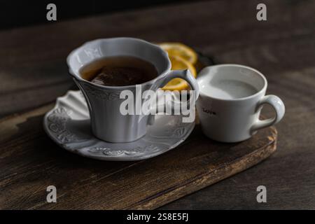 Ein klassischer englischer Tee, in einer eleganten weißen Tasse, mit Zitronenscheiben und einer Seite Milch in einer kleinen Kanne, präsentiert auf einem rustikalen Holztablett. Stockfoto