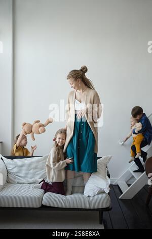Eine fröhliche Familienszene mit einer Mutter und vier Kindern, die in einem gemütlichen Wohnzimmer spielen. Die Kinder werden spielerisch aktiv und sorgen für eine warme Atmosphäre Stockfoto