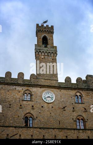 Eine Nahaufnahme des Priori-Palastturms in Volterra, Toskana, mit seiner mittelalterlichen Architektur und seiner berühmten Uhr. Die Steinstruktur steht hoch aga Stockfoto