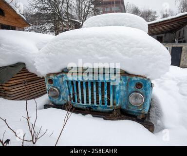 Ein alter, rostiger Truck, der teilweise unter dicken Schneeschichten versteckt ist, in einer ländlichen Winterlandschaft in Georgia. Die blaue Farbe steht im Kontrast zu der weißen Kreation Stockfoto