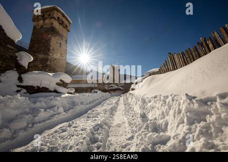 Eine malerische Winterszene eines schneebedeckten Dorfes mit alten Steintürmen in Georgien die helle Sonne scheint am klaren blauen Himmel und wirft lange Schatten Stockfoto