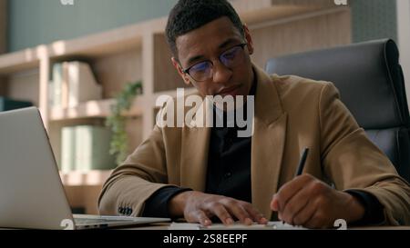 Afroamerikanischer Mann Unternehmer männlicher Geschäftsmann Buchhalter Autor Analyst schreibt Notizen Lesen Sie Informationen über Laptop zählen Geschäftsbudget schreiben Stockfoto