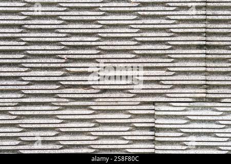 Eine strukturierte Wand aus ineinander greifenden Steinblöcken mit einem sich wiederholenden Muster aus Rillen und Graten. Die Oberfläche erscheint verwittert und grau, Creat Stockfoto