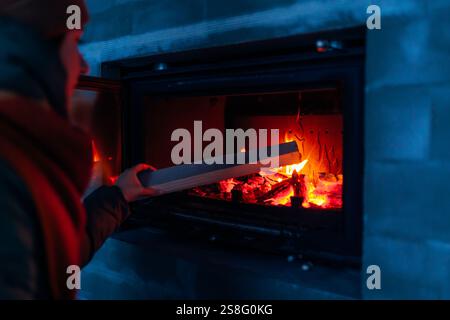 Frau, die Holz zum frisch installierten Kamin in einem neu gebauten Haus hinzufügt. Nahaufnahme des Feuers. Ein gemütliches Zuhause schaffen Stockfoto