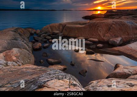 Leuchtende Farben erfüllen den Himmel über Göteborg, wenn die Sonne untergeht, und reflektieren in flachen Pools zwischen den Felsen entlang der Küste und schaffen eine ruhige Atmosphäre Stockfoto
