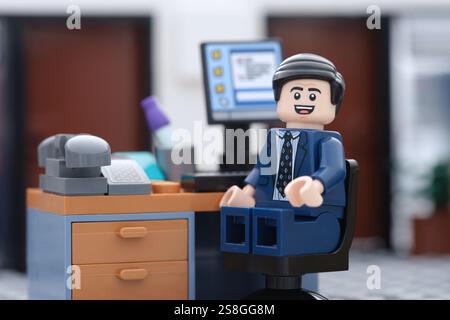 Tambow, Russische Föderation - 22. Januar 2025 Eine glückliche Lego-Geschäftsmann-Minifigur sitzt auf einem Stuhl hinter einem Computer in einem Büro und schaut sich den an Stockfoto