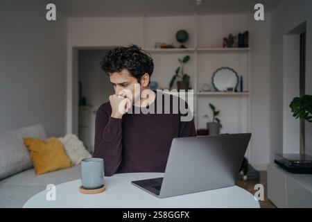 Junger, gestresster aussehender Mann aus dem Nahen Osten, der Computer benutzt und von der Arbeit überwältigt wird. Stockfoto