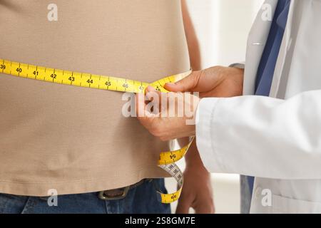 Ernährungswissenschaftler misst die Taille eines übergewichtigen Mannes mit Klebeband in der Klinik, Nahaufnahme Stockfoto