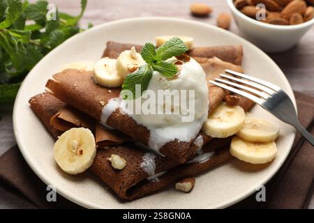 Köstliche Schokoladencrepes mit Banane, Nüssen, Minze und Eislöffel auf dem Tisch, Nahaufnahme Stockfoto