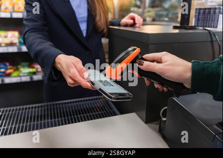 Ein Kassierer scannt einen qr-Code von einem Smartphone mit einem Strichcode-Scanner. Das Bild zeigt eine moderne kontaktlose Zahlungsmethode im Einzelhandel Stockfoto