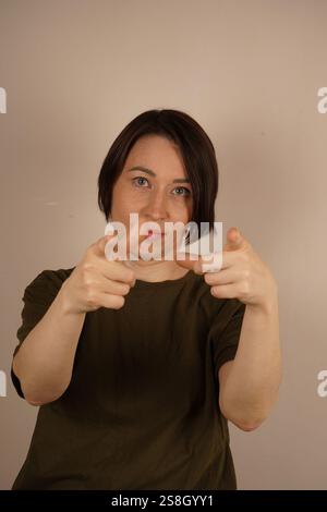 Die Frau schaut direkt in die Kamera und zeigt mit ihren Zeigefingern in die Richtung, in die sie blickt. Nahaufnahme. Auf einem isolierten Grau Stockfoto
