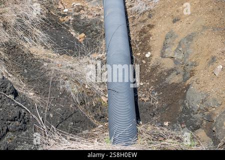 Ein Rohr liegt im Schmutz, mit einem grasbewachsenen Bereich darüber. Das Rohr ist lang und schmal und von Schmutz und Gras umgeben. Begriff der Industrie Stockfoto