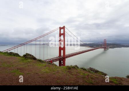Die Golden Gate Bridge steht hoch über der Bucht, umgeben von üppigen grünen Hügeln. Weiche Wolken hängen am Himmel und reflektieren das ruhige Wasser darunter. Diese VI Stockfoto