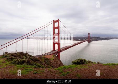 Die Golden Gate Bridge steht hoch über der Bucht, umgeben von üppigen grünen Hügeln. Weiche Wolken hängen am Himmel und reflektieren das ruhige Wasser darunter. Diese VI Stockfoto