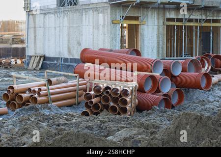 Stapel von Baurohren auf einer Baustelle mit matschigem Untergrund und unfertigen Betonwänden im Hintergrund Stockfoto
