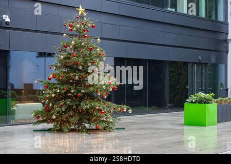 Wunderschön dekorierter Weihnachtsbaum mit roten und goldenen Ornamenten, leuchtenden Lichtern und einem goldenen Stern auf der Oberseite bei leichtem Regen Stockfoto