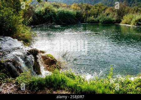 Krka Nationalpark, Šibenik-Knin – HR - 17. Oktober 2024 Ein ruhiger Ort, an dem ein kleiner Wasserfall in einen klaren, grünen Fluss fließt, umgeben von üppigem Vegetati Stockfoto