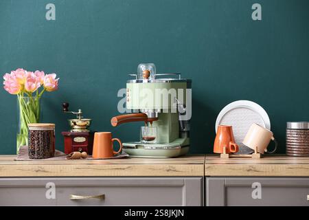Moderne Kaffeemaschine mit einem Glas heißem Espresso und einem Glas Bohnen auf der Theke in der Nähe der grünen Wand in der Küche Stockfoto