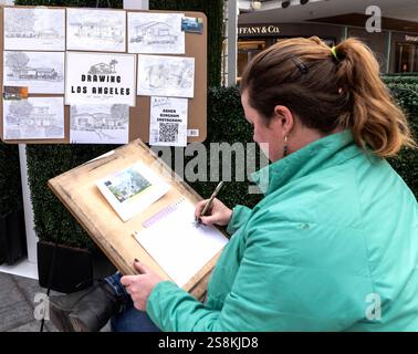 Los Angeles, Kalifornien, USA. Januar 2025. Die Künstlerin ASHER BINGHAM arbeitet auf einem Foto von Google Street View und beginnt mit der Arbeit an einer Skizze eines Altadena-Hauses, das beim Eaton-Brand zerstört wurde. Obwohl sie in der Regel von zu Hause aus arbeitet, nimmt Frau Bingham heute an einer Veranstaltung „We Love LA“ in der Westfield Century City Mall Teil, die von FIGS, einer medizinischen Uniformen- und Bekleidungsfirma mit Sitz in Santa Monica, gesponsert wird. Ms. Bingham begann mit dem Zeichnen verbrannter Häuser mit einer Zeichnung eines Hauses, das von einem Freund verloren ging. Bald verbreitete sich die Nachricht, dass sie sich bemühte, Feueropfern eine Erinnerung zu geben, und sie hat jetzt eine stabile o Stockfoto
