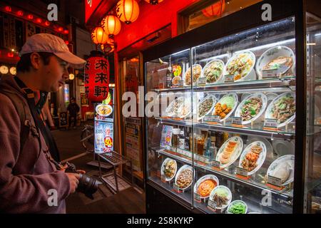 Ein Mann, der nachts in ein Restaurantfenster schaut, mit Essensproben im Akabane-Viertel von Tokio, Japan. Stockfoto
