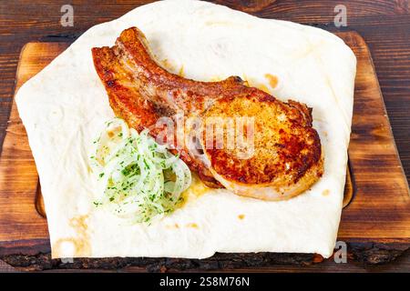 Perfekt gegrillte Rippchen ruhen auf einem warmen Fladenbrot, garniert mit dünn geschnittenen Zwiebeln und Kräutern. Dieses Gericht ist ideal für eine zwanglose Dining-Tour Stockfoto