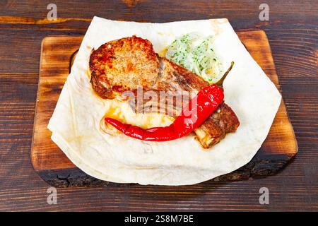 Ein saftiges gegrilltes Rippenstück liegt auf einem Holzbrett, gekrönt mit einer lebendigen Chili-Pfeffer und würzigen Kräutern. Perfekt vorbereitet und bereit für einen Stockfoto