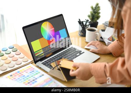 Eine Innenarchitektin, die an ihrem Schreibtisch mit Farbmustern, Designskizzen und einem Laptop mit Farbrad arbeitet Stockfoto