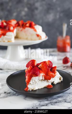 Ein köstliches Stück pavlova garniert mit Schlagsahne, frischen Erdbeeren und Erdbeersauce serviert auf einem schwarzen Teller mit dem kompletten Dessert im Stockfoto