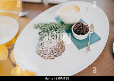 Ein Dessertteller mit einem Dessert und einer Sauce. Das Dessert ist ein Kuchen mit Puderzucker drauf. Die Platte steht auf einem Tisch Stockfoto