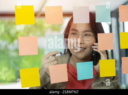 Geschäftsfrau mit Smartphone und Schreiben auf Post-IT-Notizen, Brainstorming-Sitzung mit Post-IT-Notizen im Büro. Selektiver Fokus. Stockfoto