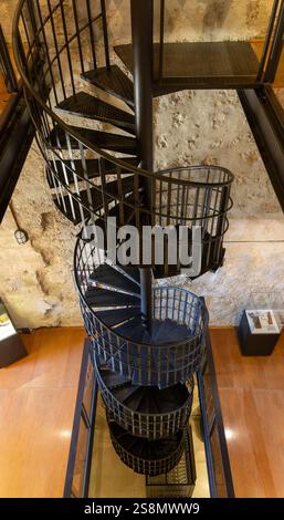 Eine Wendeltreppe ist in einem Gebäude mit einer Steinmauer zu sehen. Die Treppe ist aus Metall und hat eine schwarze Farbe. Die Treppe ist sehr hoch und hat Stockfoto