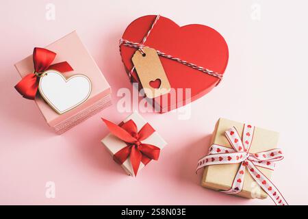 Verschiedene Geschenkboxen mit roten Bändern und Herzdekorationen auf einem sanften rosa Hintergrund. Valentinstag-Konzept. Draufsicht, flach. Stockfoto