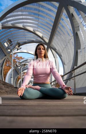 Fitnesslehrer meditiert in Lotuspositionen auf einer modernen Metallbrücke und genießt einen Moment der Achtsamkeit und Entspannung Stockfoto