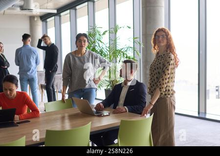 Ein vielseitiges Team von Geschäftsleuten und dem Unternehmensleiter, das geschäftliche Erfolge auf einem Laptop in einem modernen Büro überprüft und diskutiert Stockfoto