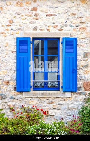 Fenster mit blauen Fensterläden auf einem idyllischen Ferienhaus und Blumen im Garten Stockfoto
