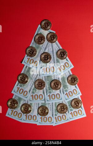 Weihnachtsbaum aus 100-Dollar-Scheinen und Bitcoin-Kryptowährungsmünzen auf rotem Hintergrund, Nahaufnahme. Weihnachtliche Einrichtung zum Thema Finanzen, Sparen Stockfoto