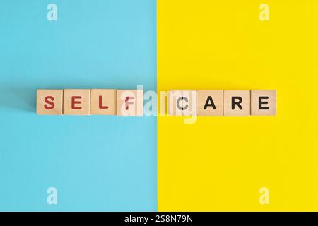 Selbstpflege-Erinnerung und Bewusstsein Holzblöcke Typografie auf hellblauem und gelbem Hintergrund. Stockfoto