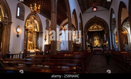 Ein historisches Kircheninnere mit Holzbänken, verzierten Altären und gotischen Bögen. Die warme Beleuchtung unterstreicht die detaillierten religiösen Kunstwerke und die großen Archi Stockfoto