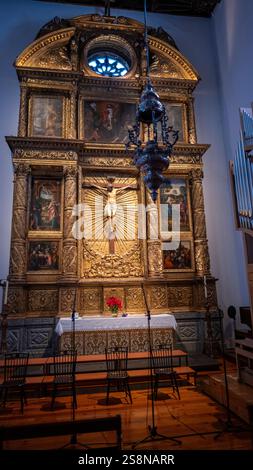 Ein kunstvoller goldener Kirchenaltar mit einem Kruzifix in der Mitte, umgeben von religiösen Gemälden und komplizierten Schnitzereien unter sanfter Innenbeleuchtung Stockfoto