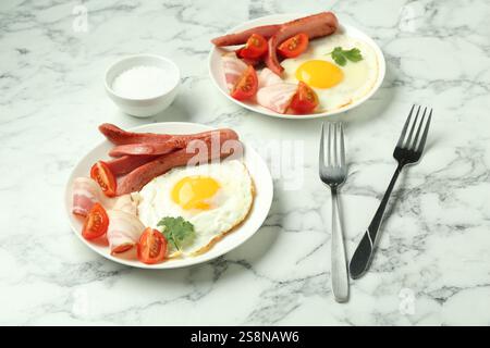 Leckerer Brunch. Spiegeleier, Würstchen, Speck und Tomaten werden auf weißem Marmortisch serviert Stockfoto