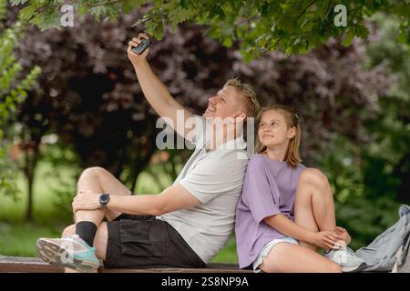Vater und Tochter machen Ein Selfie auf Einer Sommerbank und genießen die gemeinsame Familienzeit Stockfoto