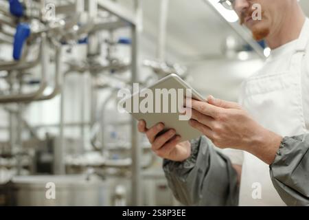 Männlicher Fachmann, der industrielle Betriebsabläufe mit einem modernen Tablet in der Hand inspiziert. Konzentrieren Sie sich auf die Gewährleistung von Prozesseffizienz und Sicherheit beim Tragen von Schutzkleidung in einer Fabrikumgebung Stockfoto
