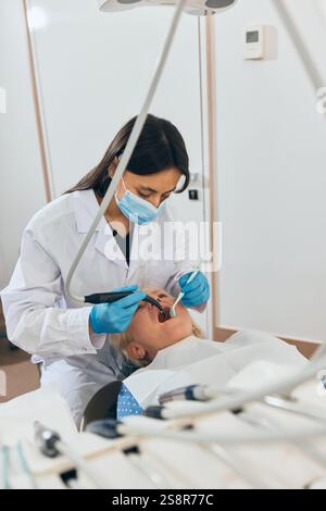 Ärztin mit Handschuhen und Maske, mit Zahnwerkzeugen bei der Untersuchung des Mundes einer älteren Frau, die auf einem Zahnstuhl liegt, in einer hellen Zahnarztpraxis. Stockfoto