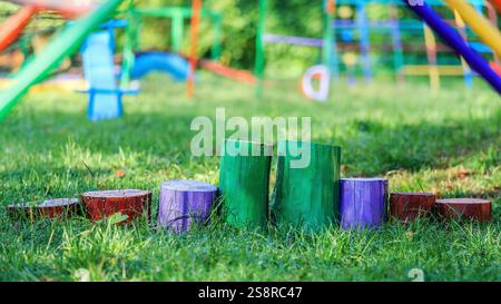 Lebhaft bemalte Holzstümpfe auf grünem Gras auf einem Spielplatz im Freien mit farbenfroher Ausrüstung im Hintergrund. Stockfoto